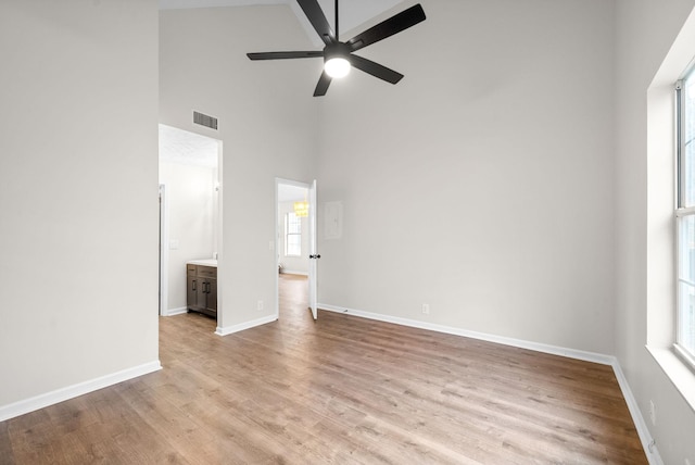 empty room with ceiling fan, a high ceiling, and light hardwood / wood-style flooring