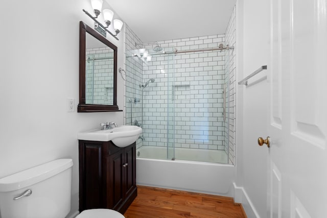 full bathroom featuring wood-type flooring, bath / shower combo with glass door, toilet, and vanity