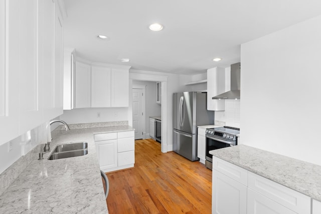 kitchen featuring light hardwood / wood-style floors, sink, appliances with stainless steel finishes, white cabinets, and wall chimney exhaust hood