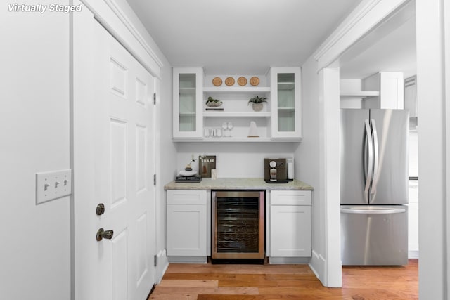 bar featuring wine cooler, stainless steel refrigerator, light wood-type flooring, white cabinets, and light stone counters