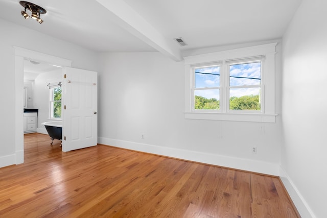 spare room with beam ceiling and light hardwood / wood-style flooring