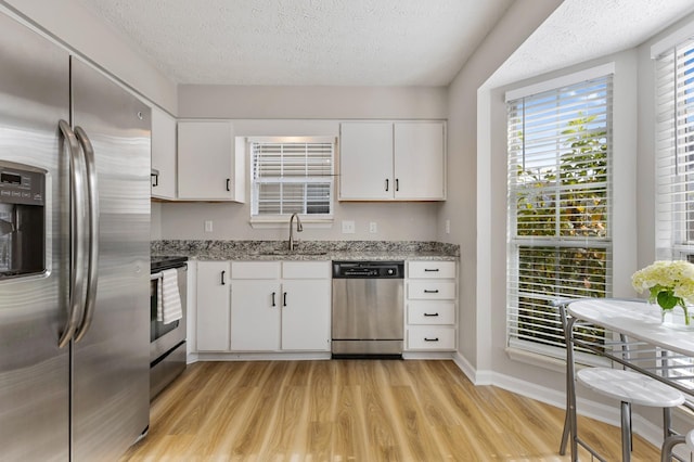 kitchen featuring light wood-type flooring, stainless steel appliances, white cabinetry, and light stone counters