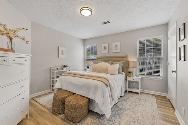 bedroom with a textured ceiling, multiple windows, and light hardwood / wood-style floors