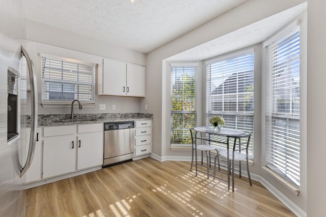 kitchen with stainless steel appliances, a textured ceiling, white cabinets, light stone counters, and sink