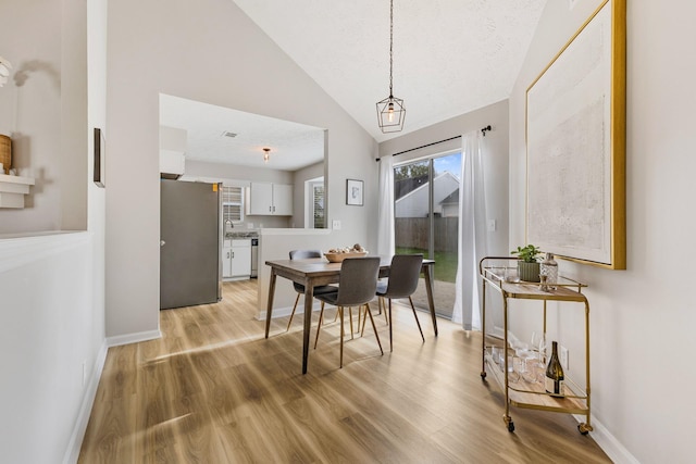 dining area with high vaulted ceiling and light hardwood / wood-style flooring