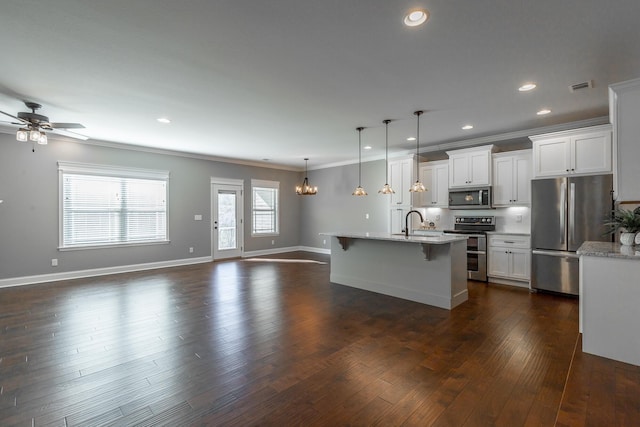 kitchen with white cabinets, appliances with stainless steel finishes, an island with sink, hanging light fixtures, and light stone counters