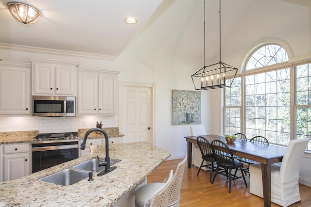 kitchen with tasteful backsplash, sink, white cabinetry, hanging light fixtures, and stainless steel appliances