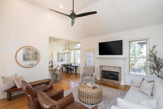 living room featuring ceiling fan, a fireplace, light hardwood / wood-style flooring, and high vaulted ceiling