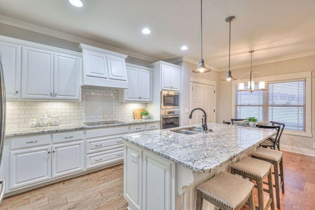 kitchen featuring white cabinetry, stainless steel appliances, an island with sink, sink, and light hardwood / wood-style flooring