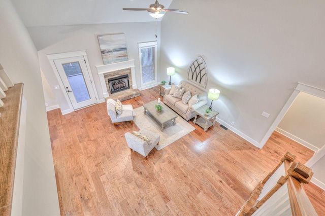 living room featuring ceiling fan, vaulted ceiling, a fireplace, and light hardwood / wood-style flooring