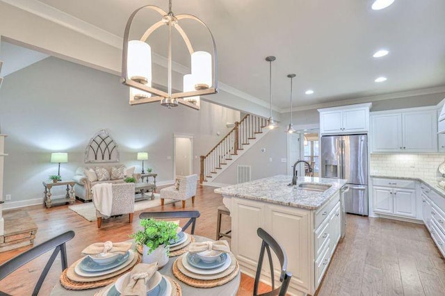 kitchen featuring stainless steel fridge with ice dispenser, white cabinets, a center island with sink, and sink