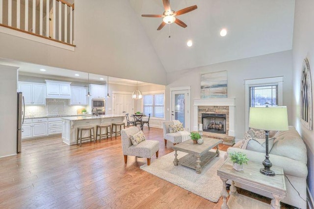 living room with ceiling fan, a fireplace, light hardwood / wood-style floors, sink, and high vaulted ceiling