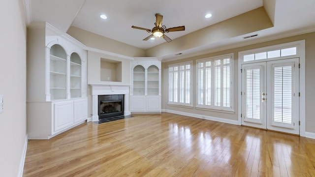 unfurnished living room with built in features, a fireplace, ornamental molding, ceiling fan, and light hardwood / wood-style flooring