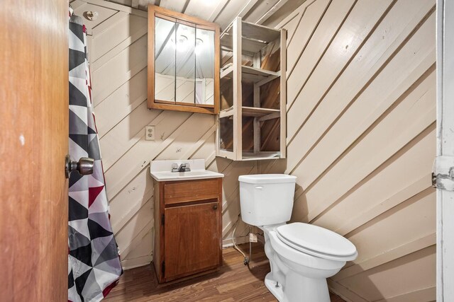 bathroom featuring toilet, wood-type flooring, wooden walls, and vanity