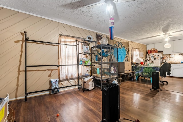 workout area with ceiling fan, wooden walls, and a textured ceiling