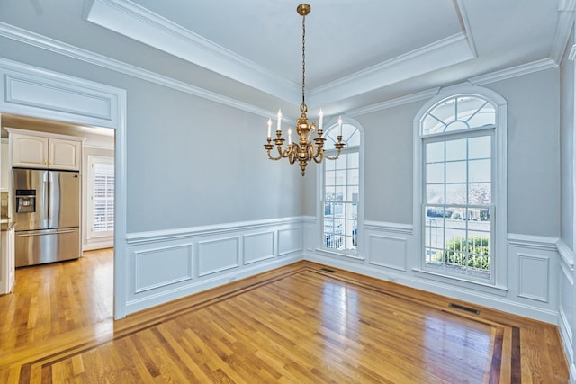 unfurnished dining area with a raised ceiling, a chandelier, ornamental molding, and light hardwood / wood-style flooring