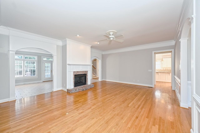 unfurnished living room with light hardwood / wood-style floors, decorative columns, ceiling fan, a fireplace, and ornamental molding