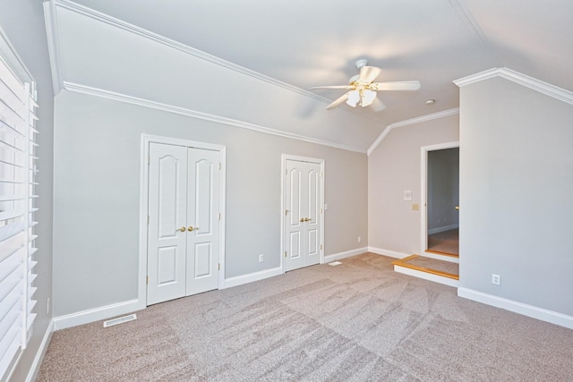 unfurnished bedroom with lofted ceiling, two closets, light carpet, ceiling fan, and crown molding