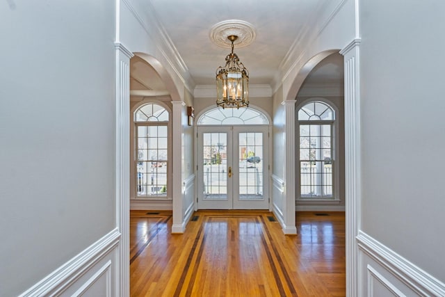 foyer entrance with a chandelier, crown molding, french doors, and decorative columns