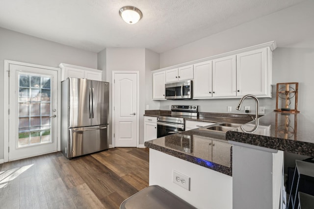 kitchen with kitchen peninsula, sink, white cabinetry, dark wood-type flooring, and appliances with stainless steel finishes