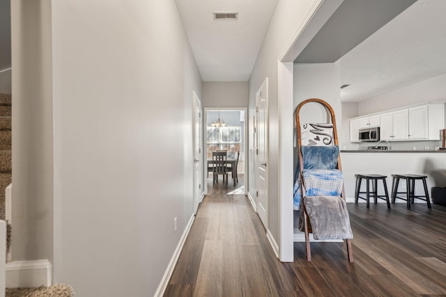 corridor with dark hardwood / wood-style flooring and a notable chandelier