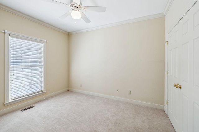 carpeted spare room with ceiling fan, a healthy amount of sunlight, and ornamental molding