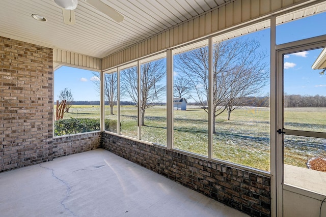 unfurnished sunroom with ceiling fan and a rural view