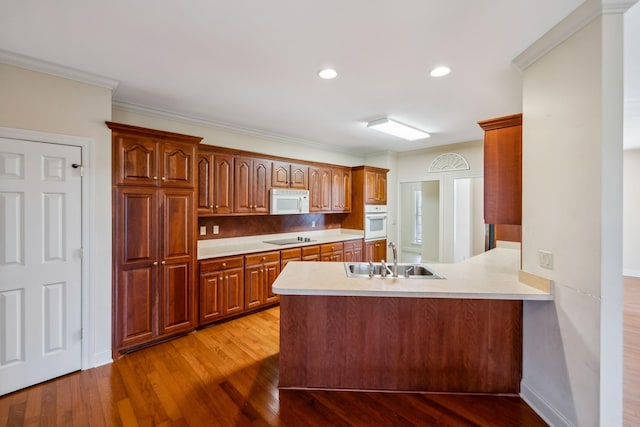 kitchen with kitchen peninsula, sink, crown molding, white appliances, and light hardwood / wood-style flooring