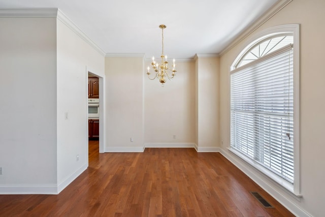 unfurnished room featuring dark wood-type flooring, a wealth of natural light, crown molding, and an inviting chandelier