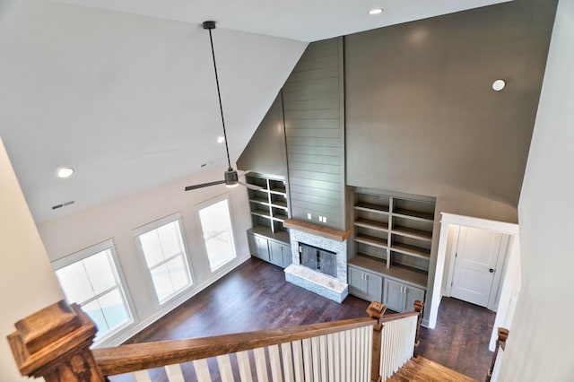 living room featuring dark wood-type flooring, a stone fireplace, built in features, high vaulted ceiling, and ceiling fan