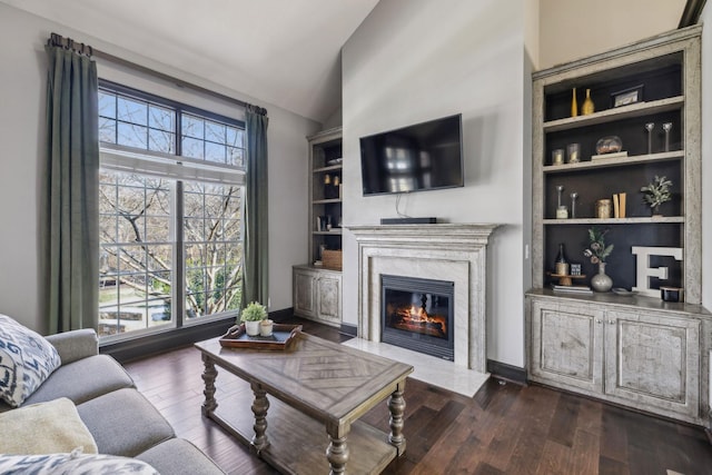 living room featuring lofted ceiling, built in features, dark hardwood / wood-style flooring, and a premium fireplace