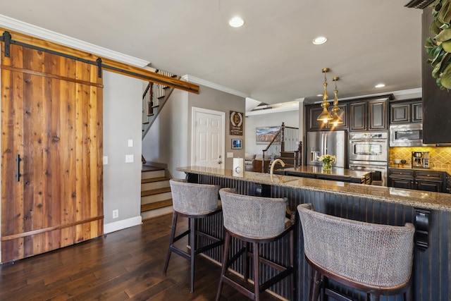 kitchen featuring pendant lighting, appliances with stainless steel finishes, a kitchen breakfast bar, crown molding, and a barn door