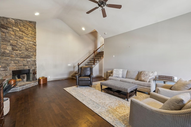 living room featuring ceiling fan, vaulted ceiling, dark wood-type flooring, and a stone fireplace