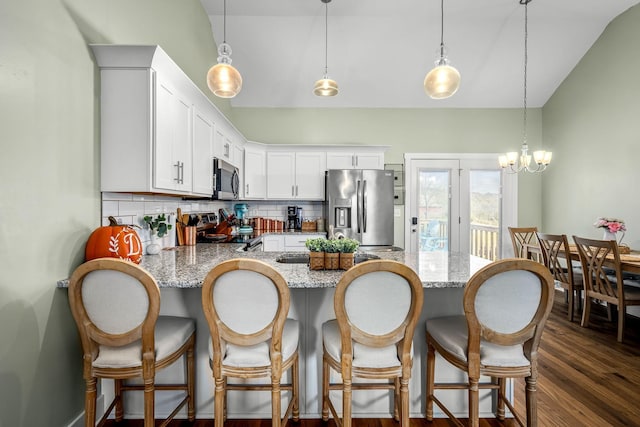 kitchen with pendant lighting, white cabinets, lofted ceiling, stainless steel appliances, and backsplash