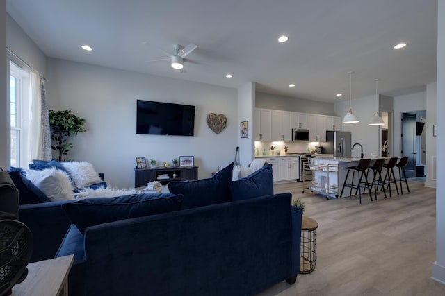 living room with light wood-type flooring, ceiling fan, and sink