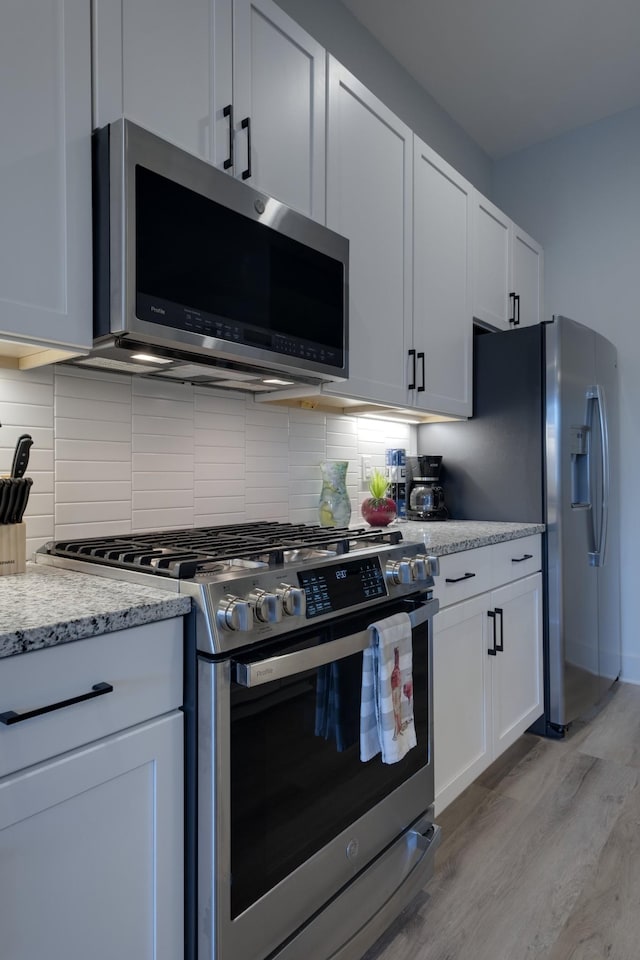kitchen featuring tasteful backsplash, light hardwood / wood-style floors, white cabinetry, appliances with stainless steel finishes, and light stone counters