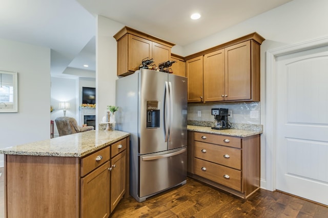 kitchen with light stone countertops, tasteful backsplash, stainless steel fridge, dark hardwood / wood-style floors, and kitchen peninsula