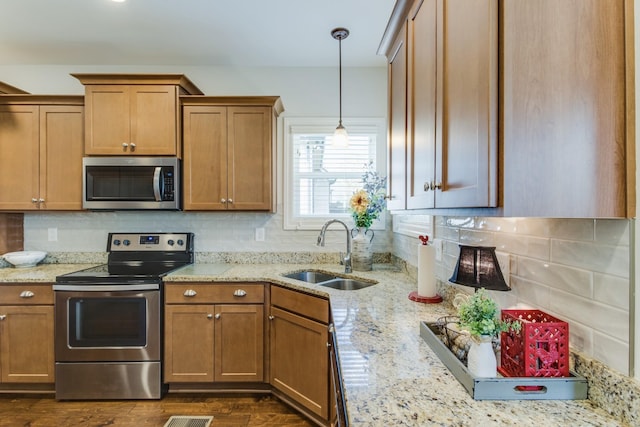 kitchen with appliances with stainless steel finishes, decorative backsplash, light stone countertops, pendant lighting, and sink