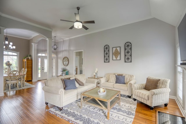 living room with ceiling fan with notable chandelier, hardwood / wood-style flooring, vaulted ceiling, decorative columns, and crown molding