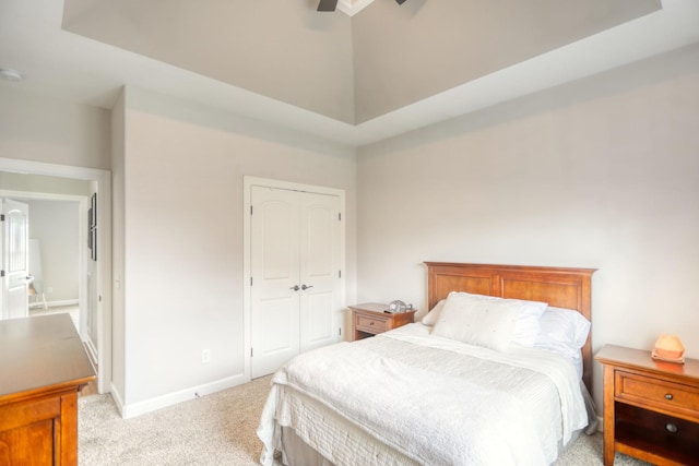 bedroom with ceiling fan, light colored carpet, a tray ceiling, and a closet