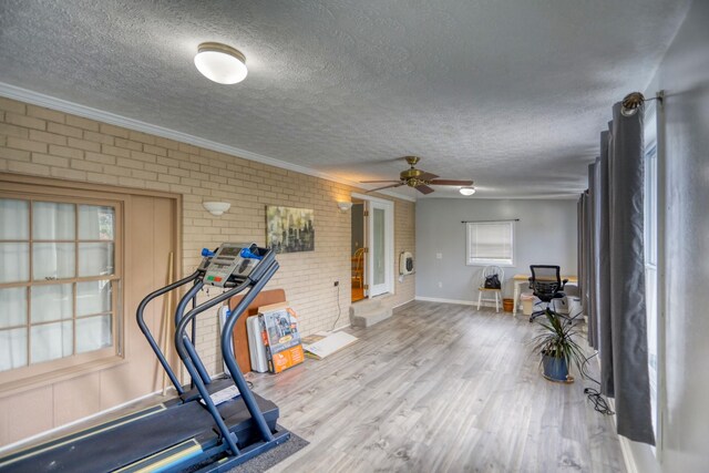 exercise room with a textured ceiling, ceiling fan, brick wall, and hardwood / wood-style floors