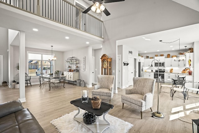 living room featuring a high ceiling, ceiling fan with notable chandelier, and light hardwood / wood-style flooring