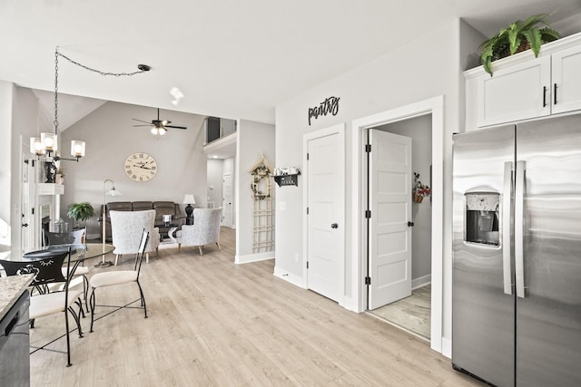 kitchen featuring stainless steel fridge with ice dispenser, white cabinetry, light wood-type flooring, vaulted ceiling, and ceiling fan with notable chandelier