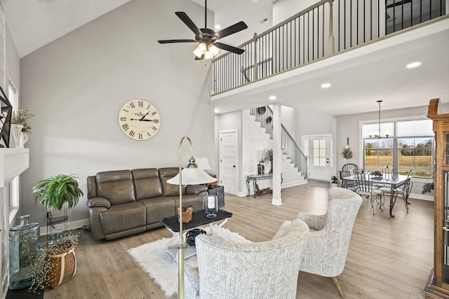 living room featuring high vaulted ceiling, ceiling fan with notable chandelier, and light wood-type flooring