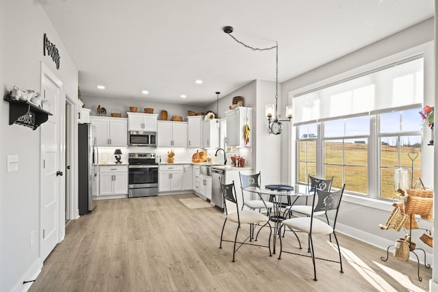 kitchen featuring decorative light fixtures, white cabinetry, stainless steel appliances, sink, and light wood-type flooring