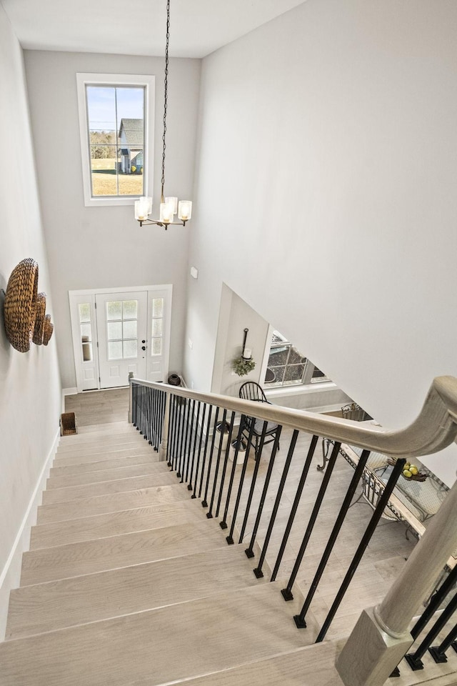 staircase featuring wood-type flooring, a high ceiling, a wealth of natural light, and an inviting chandelier