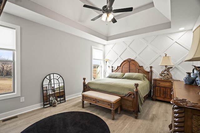 bedroom featuring ceiling fan, light hardwood / wood-style flooring, and a tray ceiling