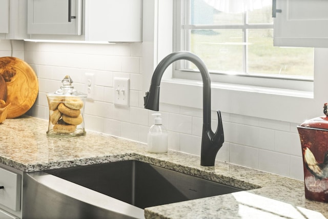 details featuring decorative backsplash, light stone countertops, white cabinetry, and sink