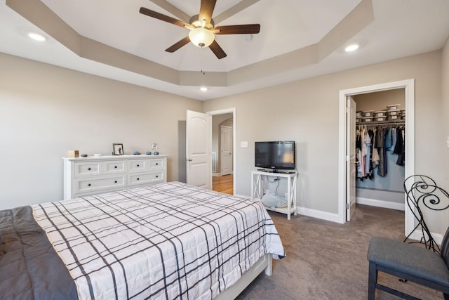 bedroom featuring a spacious closet, a tray ceiling, a closet, and ceiling fan