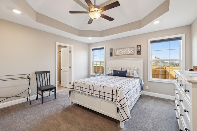 bedroom with ceiling fan, dark carpet, and a tray ceiling